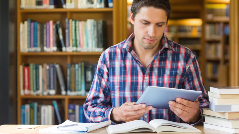 Un hombre estudia en la biblioteca con libros y tablet