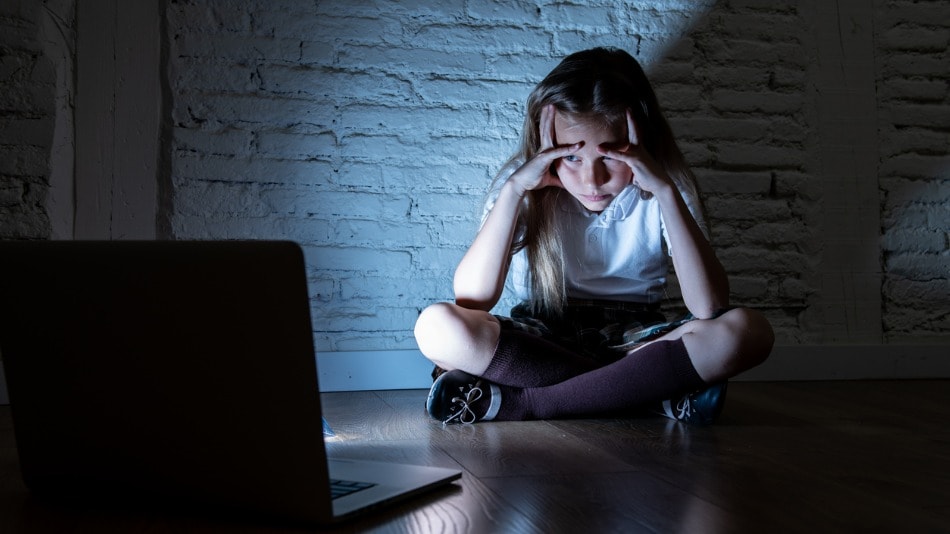 Niña víctima de ciberbullying mirando cabizbaja la pantalla de un ordenador