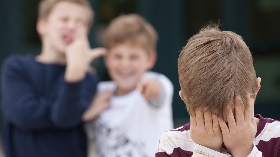 Dos niños intimidando a un tercero con la cara tapada con sus manos