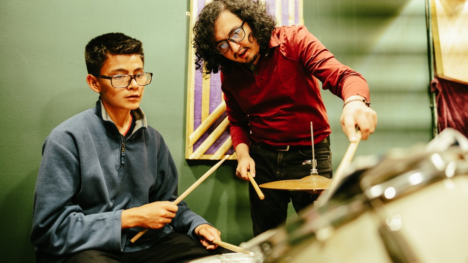 Hombre adulto enseñando batería a su alumno en un estudio de grabación