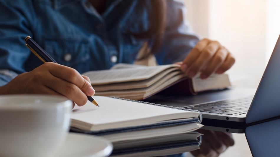 Estudiante utilizando técnicas de estudio con un ordenador, libreta de apuntes, libro y taza de café